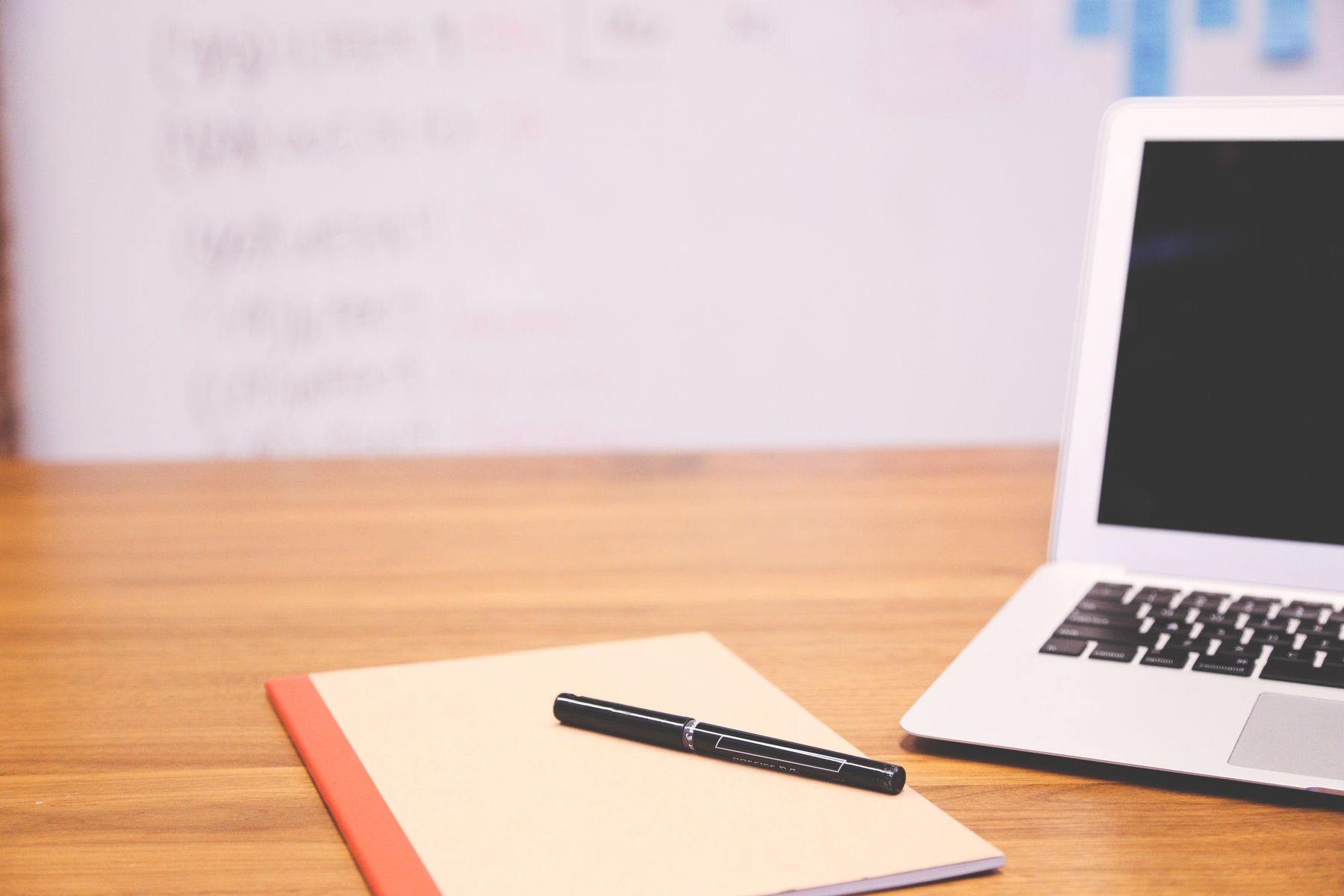 A notebook and pen beside a laptop on a desk